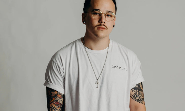 Person wearing a white t-shirt with visible tattoos on arms against a plain background