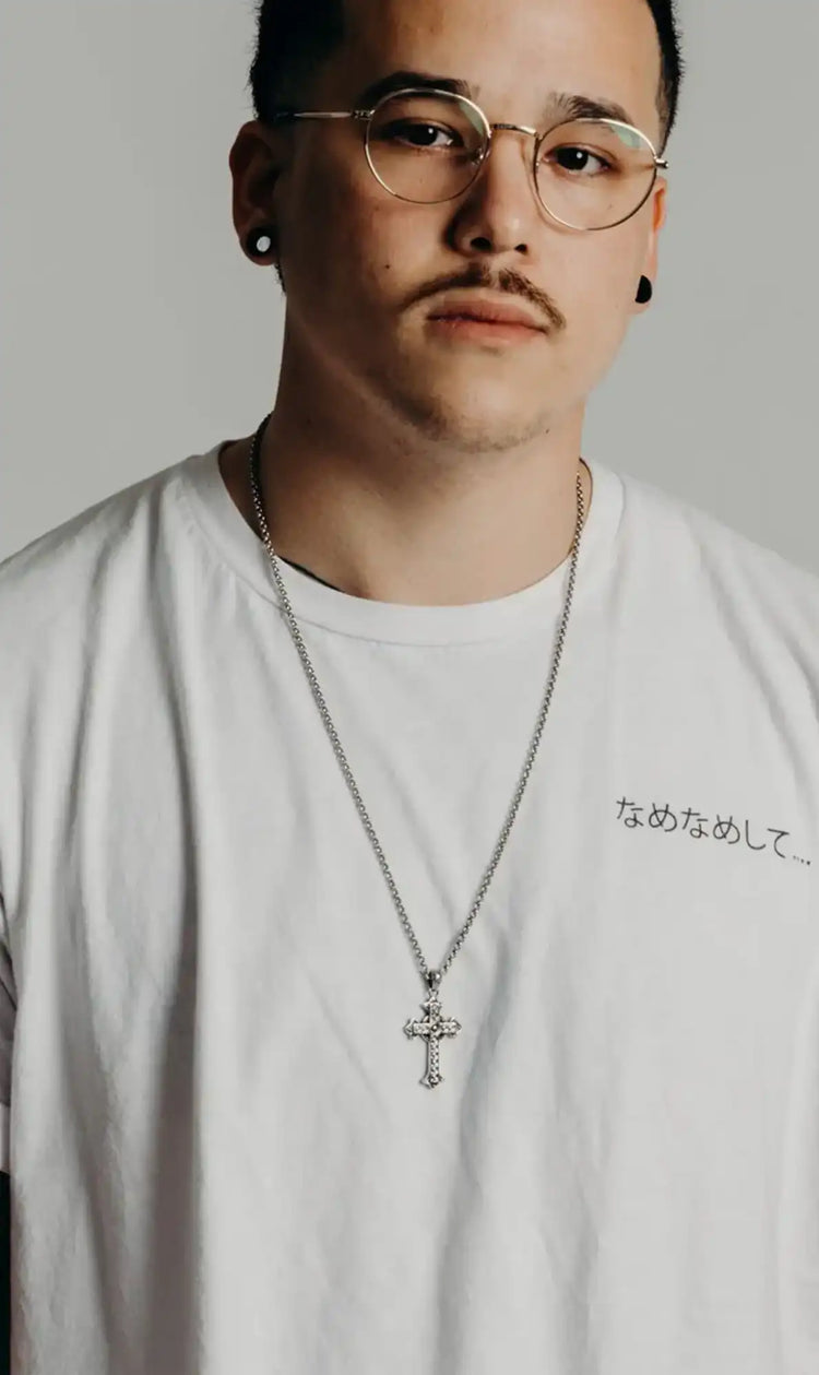 Man wearing a white t-shirt with text and a necklace with a cross pendant against a plain background